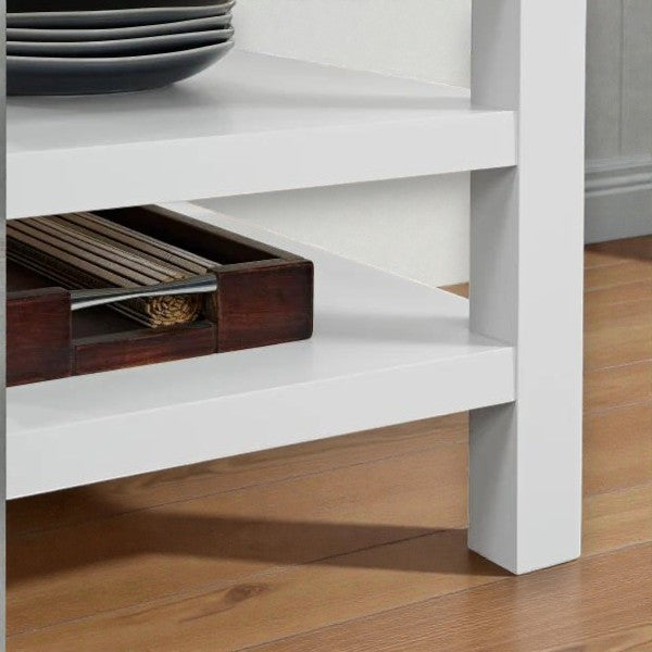 Close-up of white wooden furniture leg and lower shelf holding dark wooden tray with long, thin items on hardwood floor