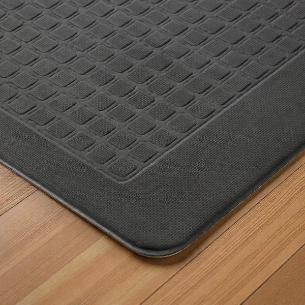 Close-up of a black anti-fatigue floor mat with textured square pattern on wooden floor