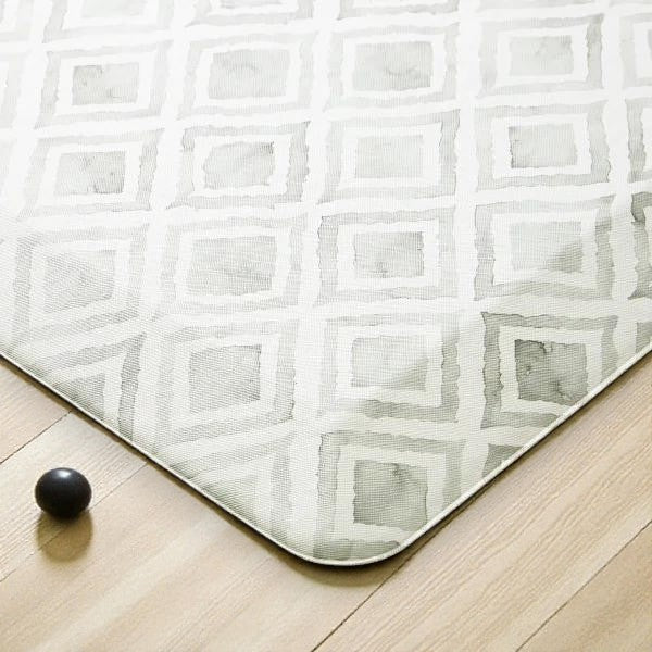 Close-up of a beige and gray geometric patterned rug on wooden floor with a small black ball nearby