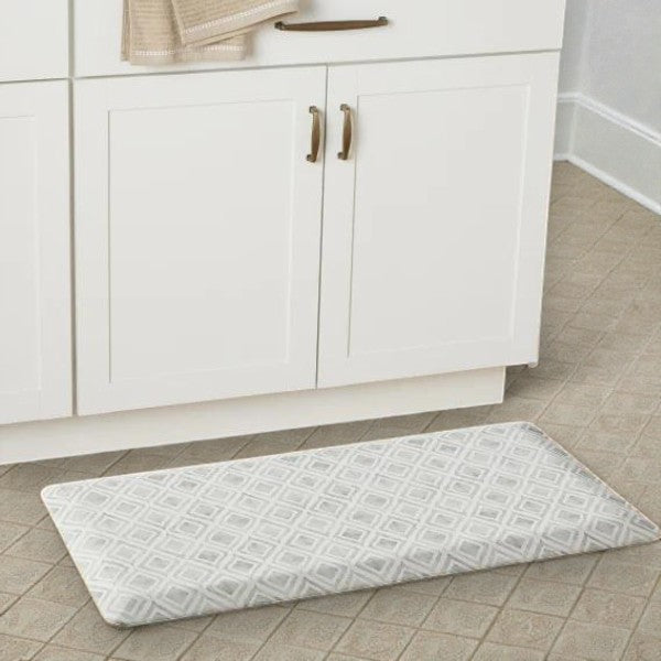 Soft gray geometric patterned kitchen floor mat in front of white cabinets with brass handles
