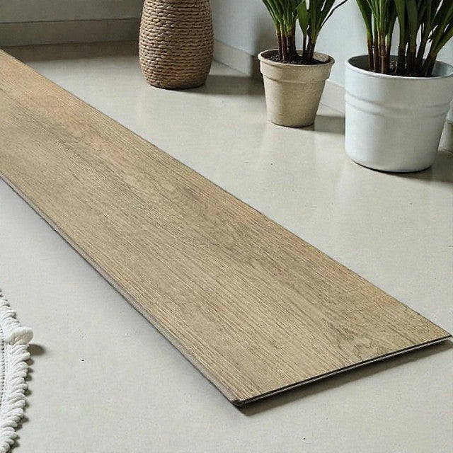 wood-look vinyl plank flooring sample on beige tile floor with potted plants and woven basket