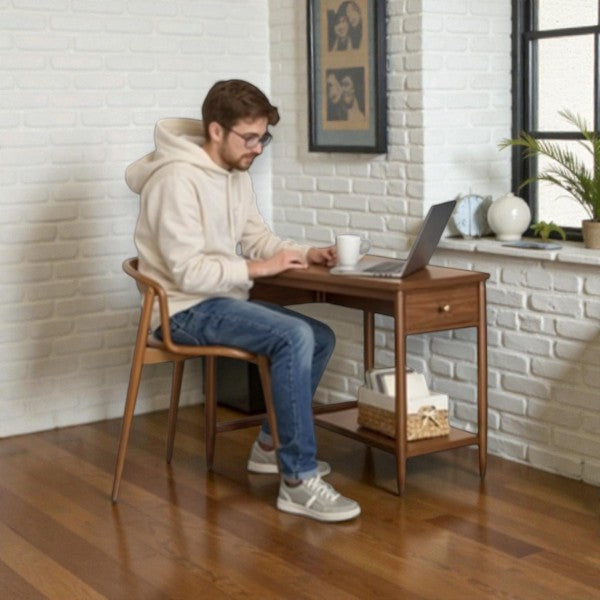 Young man in beige hoodie working on laptop at wooden desk in bright white brick room