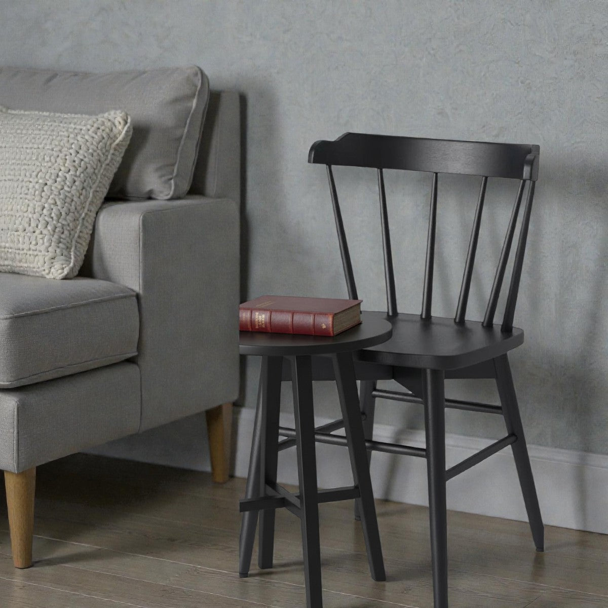 Gray sofa with knitted pillow next to black chair and small round table with vintage brown book