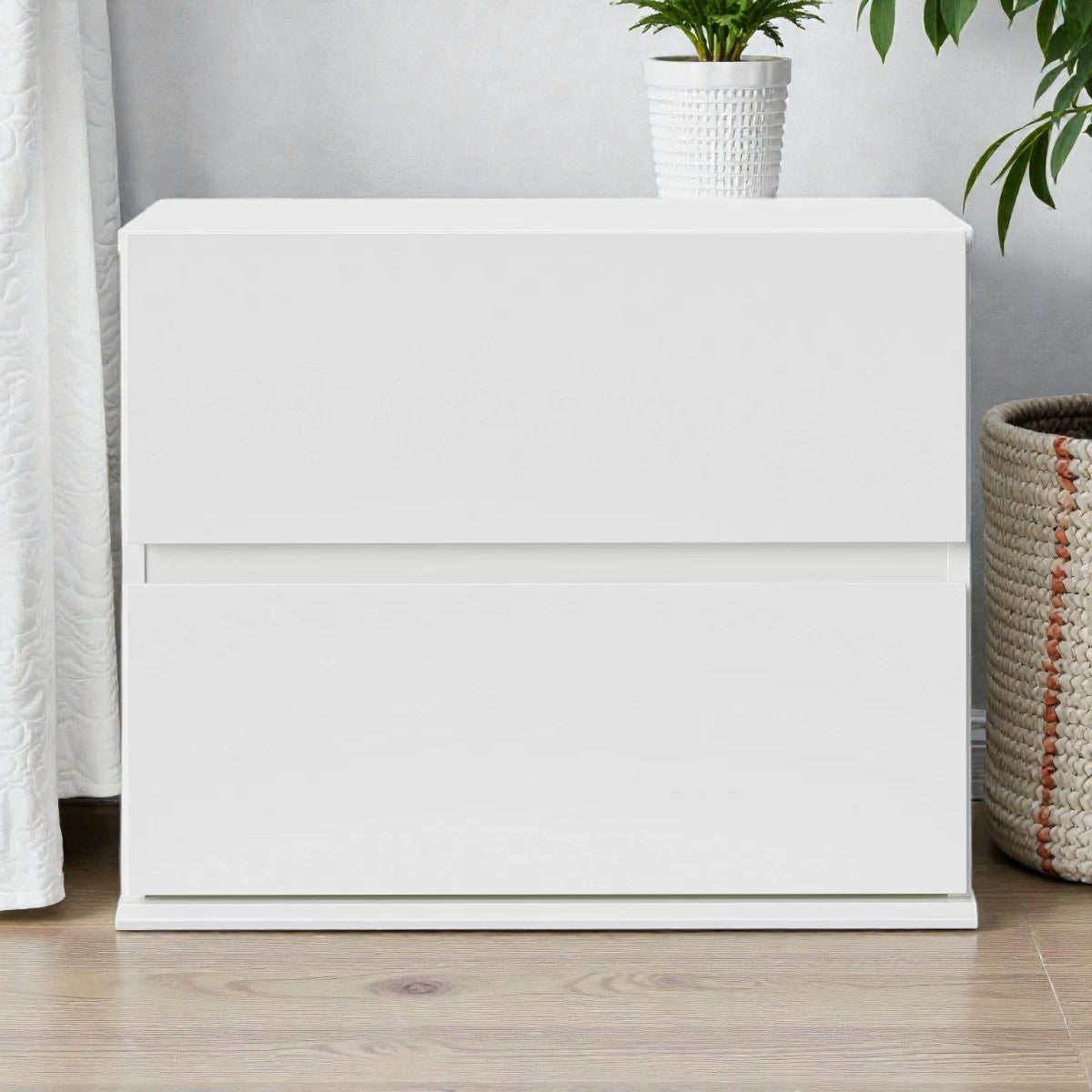 Modern white two-drawer bedside table with a white plant pot on top and wicker basket nearby