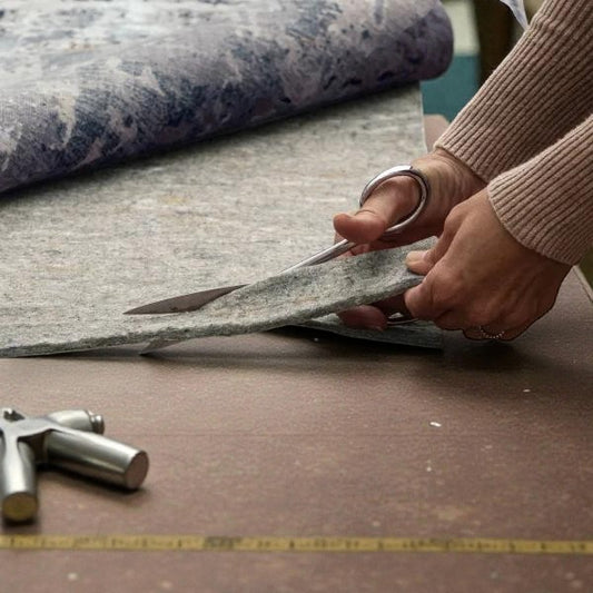 Hands cutting gray fabric with scissors on a table covered with textile tools and rolled material
