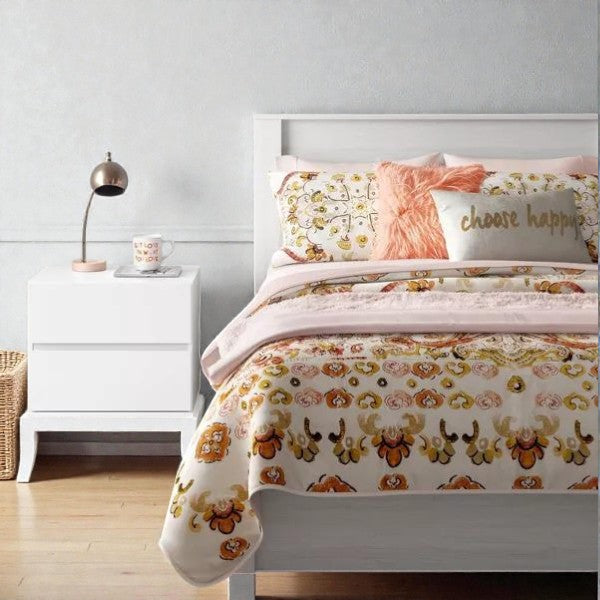 Modern white bed with floral-patterned bedding, pink throw pillow, and white nightstand with lamp and mug