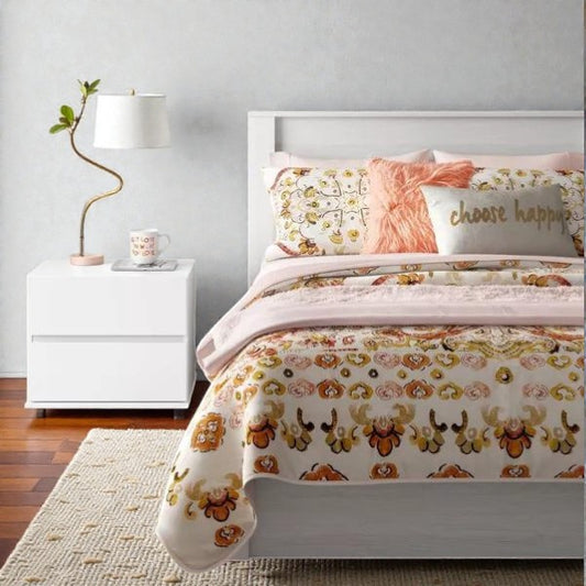 modern white bed with floral patterned bedding, pink accent pillows, white nightstand with lamp and mug on wooden floor
