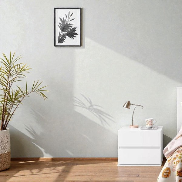 Minimalist bedroom corner with white nightstand, modern desk lamp, potted plant, and framed botanical print