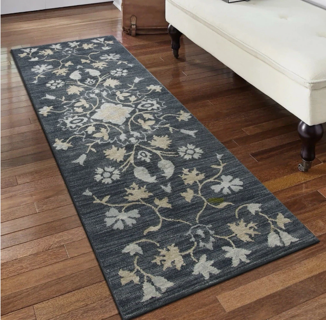Dark gray floral patterned runner rug on wooden floor beside white upholstered bench