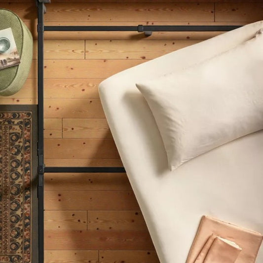 Top view of a modern bed with white pillow and beige bedding on wooden floor with patterned rug