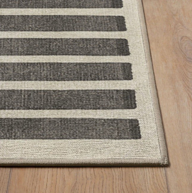 Close-up of a beige rug with dark gray horizontal stripes on a wooden floor